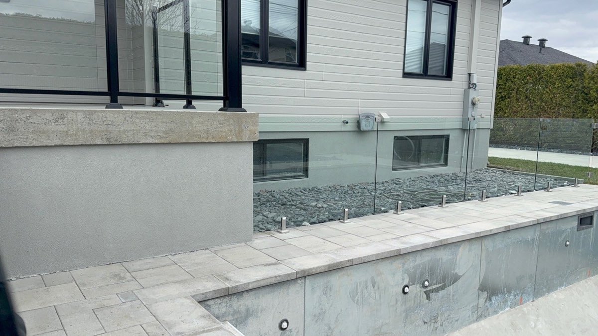 Solage et muret de piscine recouverts d'un crépi acrylique gris clair, sous un garde-corps de verre
