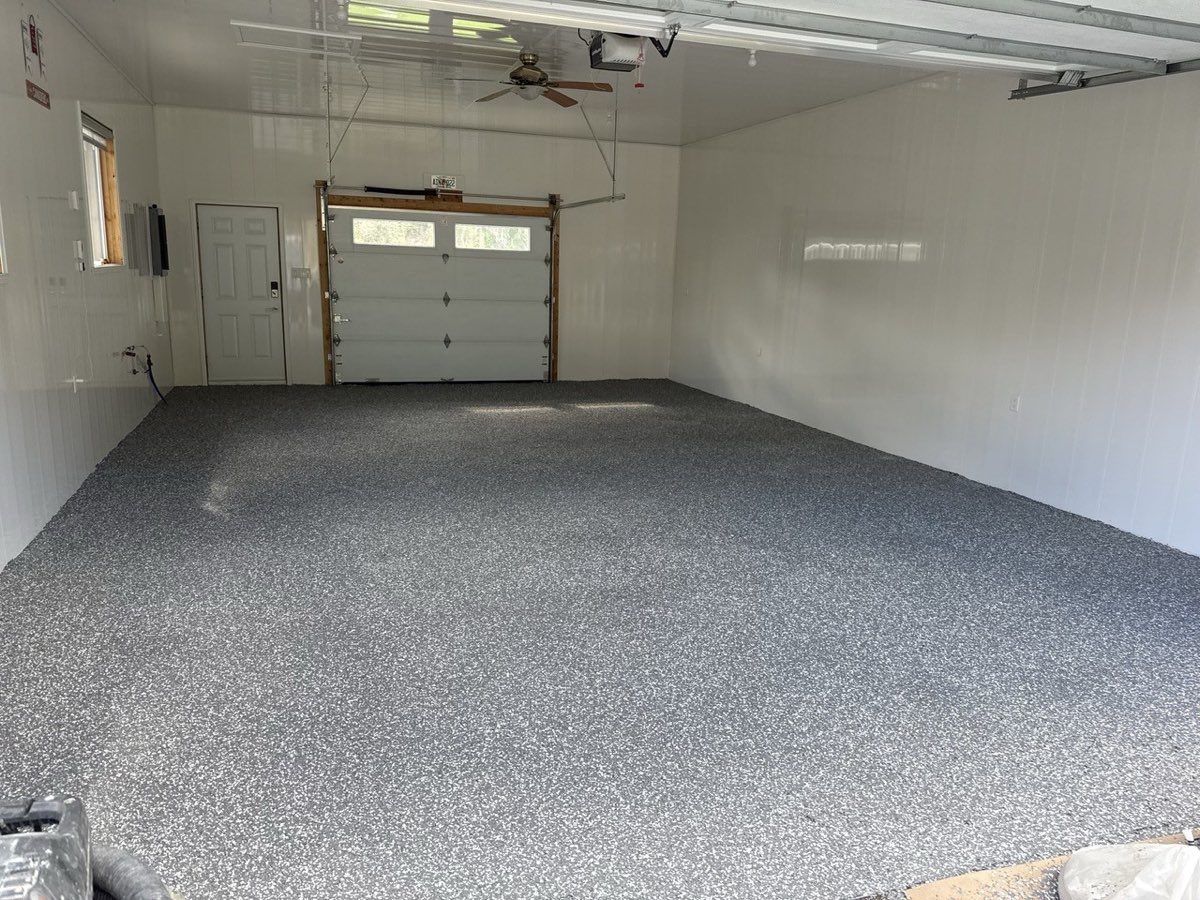 Garage résidentiel aux murs blancs, plancher époxy à flocons gris et blancs jusqu'à la porte