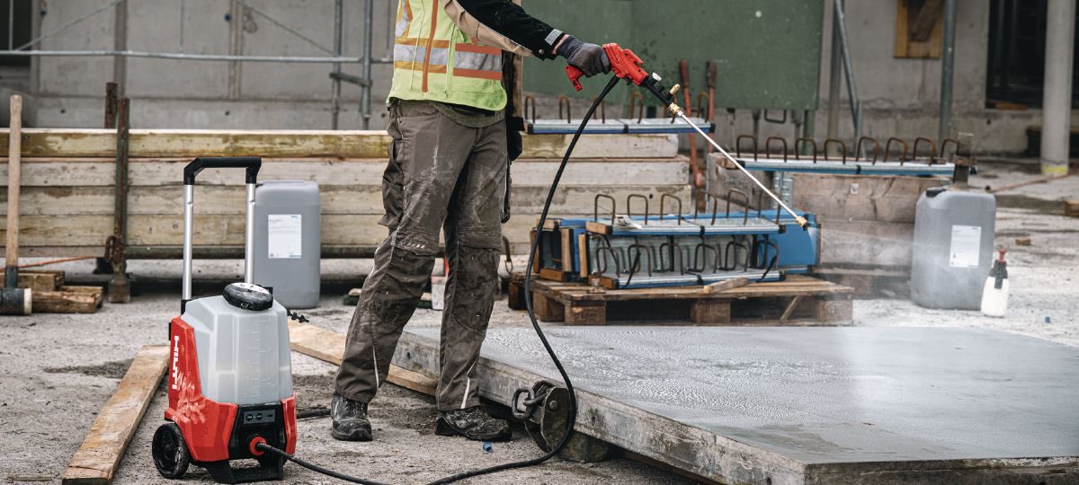 Applicateur pulvérisant un scellant sur une dalle de béton fraîchement coulée