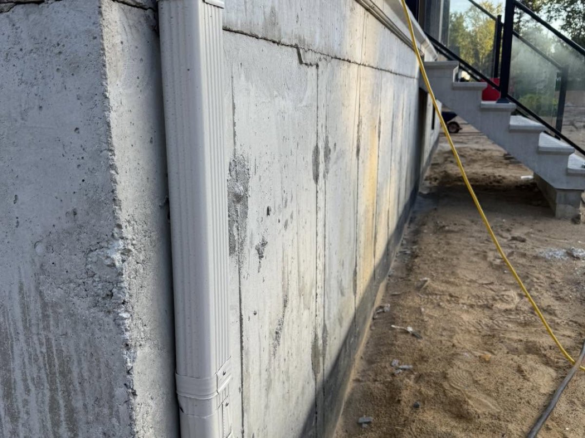 Avant les travaux, mur de fondation en béton brut le long d'une maison